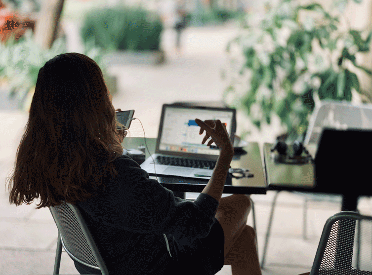 A women sitting by the table, working on a laptop, talking on the phone